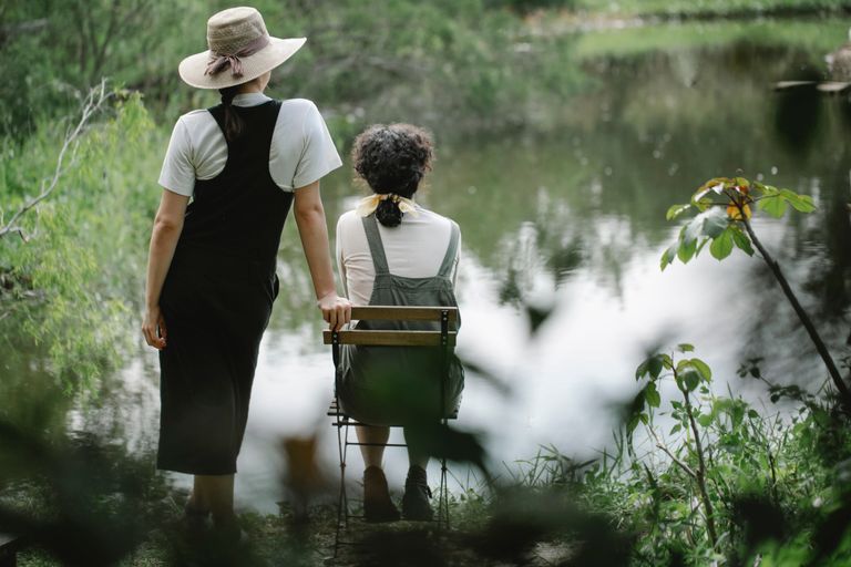 Back view full body of unrecognizable female gardeners enjoying view of lake in rural area